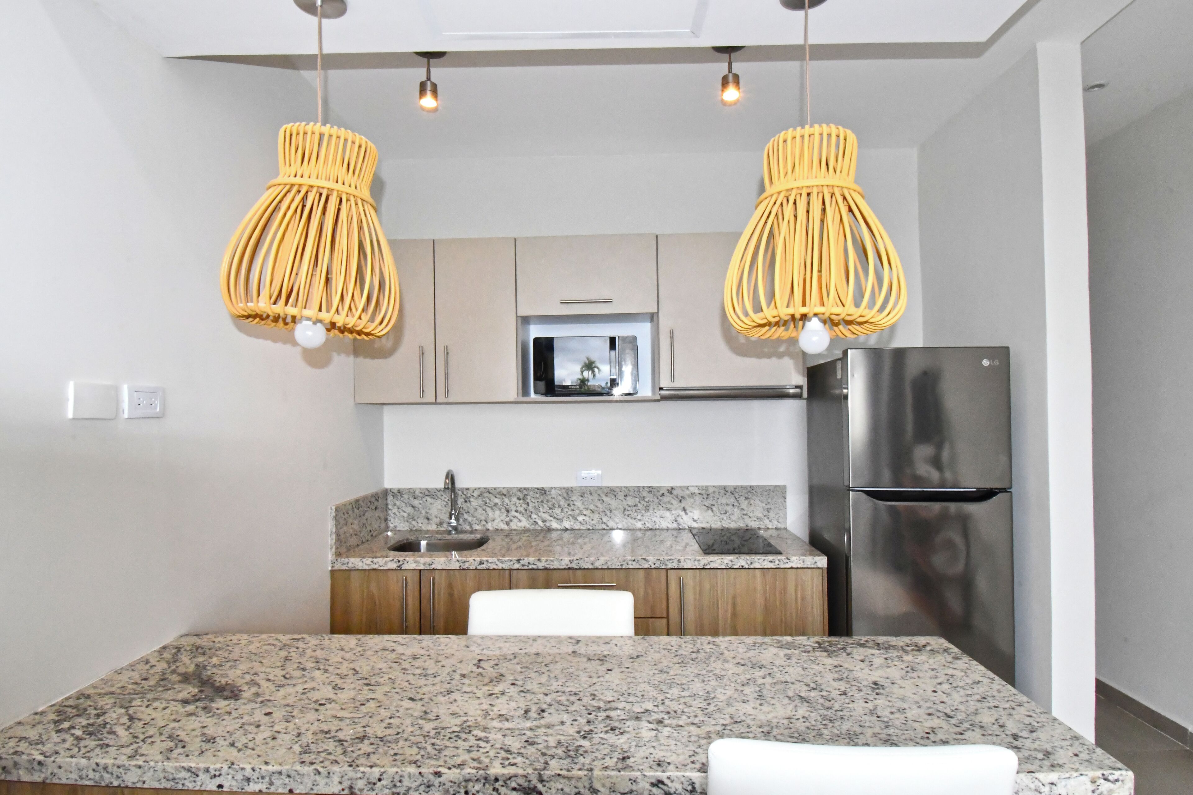 A modern kitchen with granite countertops, stainless steel appliances, and yellow woven pendant lights.