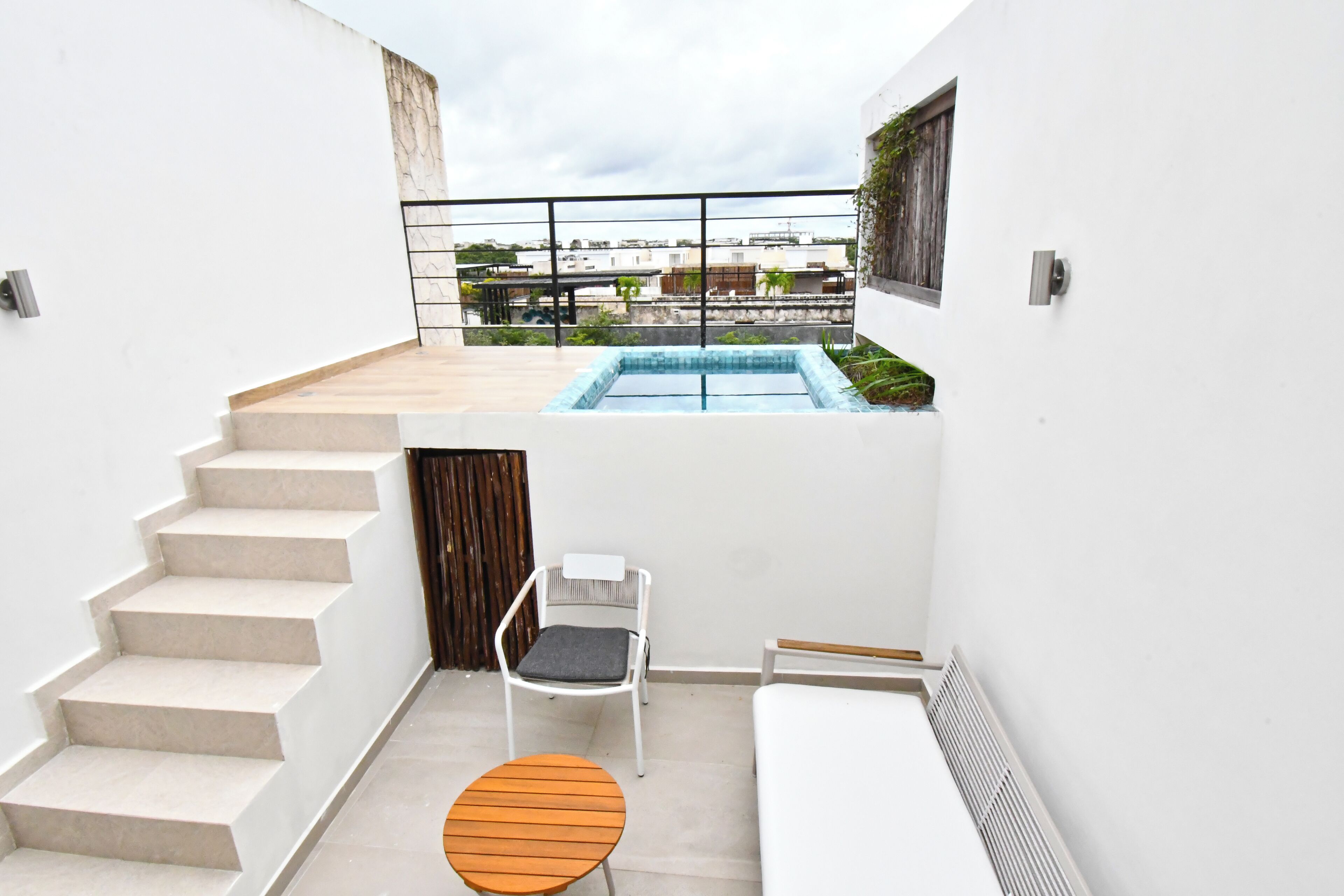 Ein kleiner, moderner Balkon mit Pool, einem Holztisch, einem weißen Stuhl und einer Treppe.