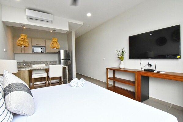 A hotel room with a bed, a desk, a TV, a kitchen area, and a dining table. - Solum Living by The Spot Rentals (Tulum)