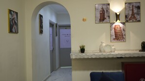 En hall med ett vitt marmorgolv, en blå soffa och ett rött skåp. På väggen hänger inramade bilder av Eiffeltornet och det lutande tornet i Pisa.