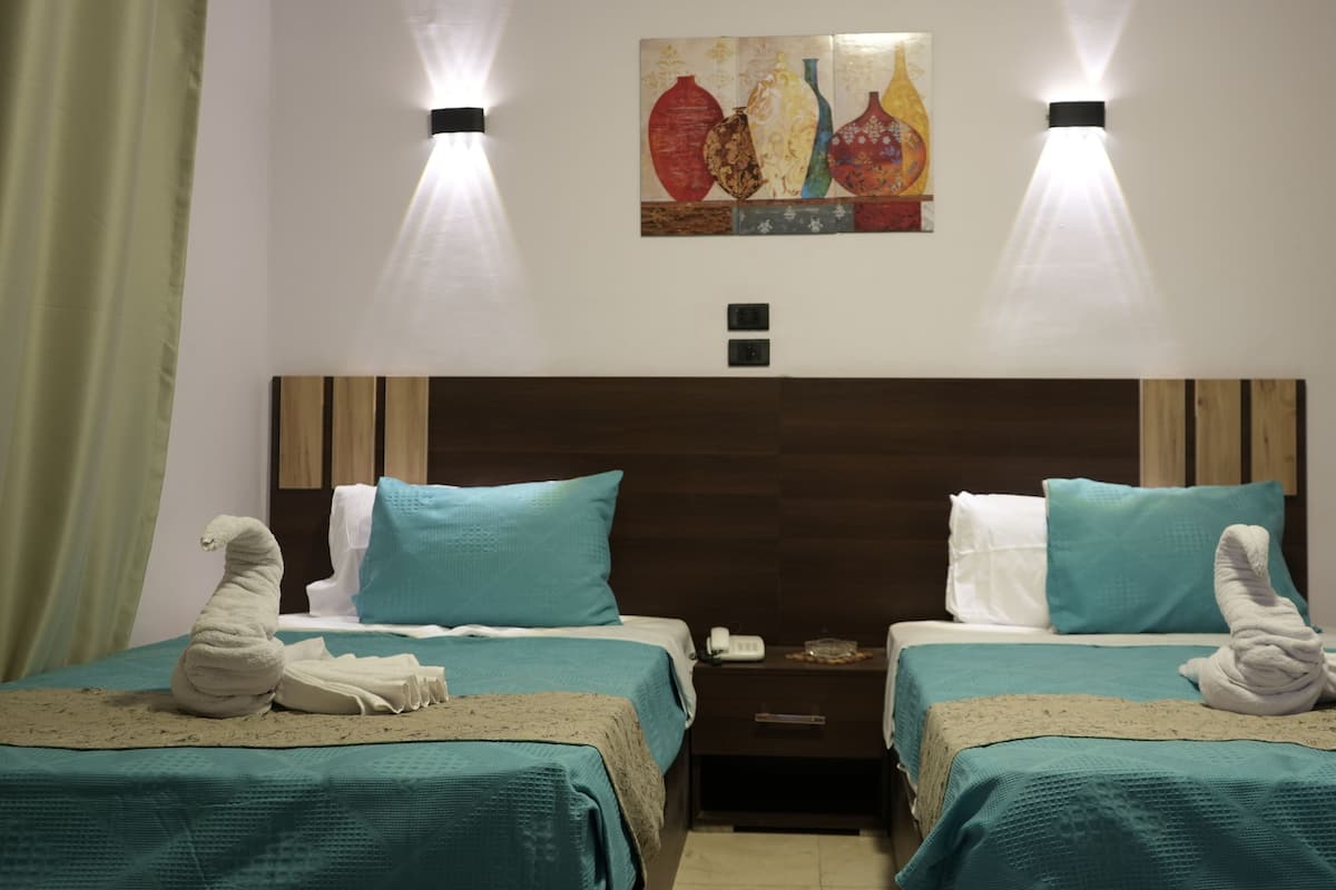 A hotel room with two beds, each with a teal bedspread and white pillows, a wooden headboard, and two wall-mounted lights.