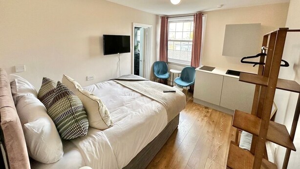 A bedroom with a bed, bedside table, TV, and a desk with chairs. - Snug studio flat in Camden (Greater London)