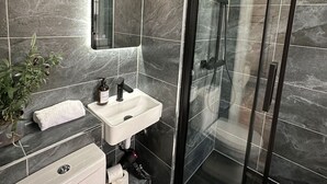 A modern bathroom with a glass shower enclosure, a white sink, and a toilet. - Snug studio flat in Camden (Greater London)