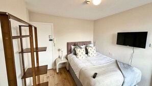 A bedroom with a bed, a TV mounted on the wall, a bedside table, and a wooden shelf unit. - Snug studio flat in Camden (Greater London)