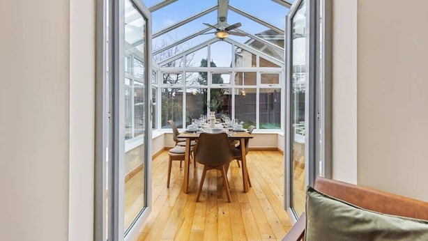 Une véranda équipée d’une table à manger pour quatre personnes, de grandes fenêtres et d’un ventilateur de plafond.