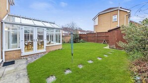 Un jardin avec une véranda, une clôture en bois et une pelouse bien entretenue.