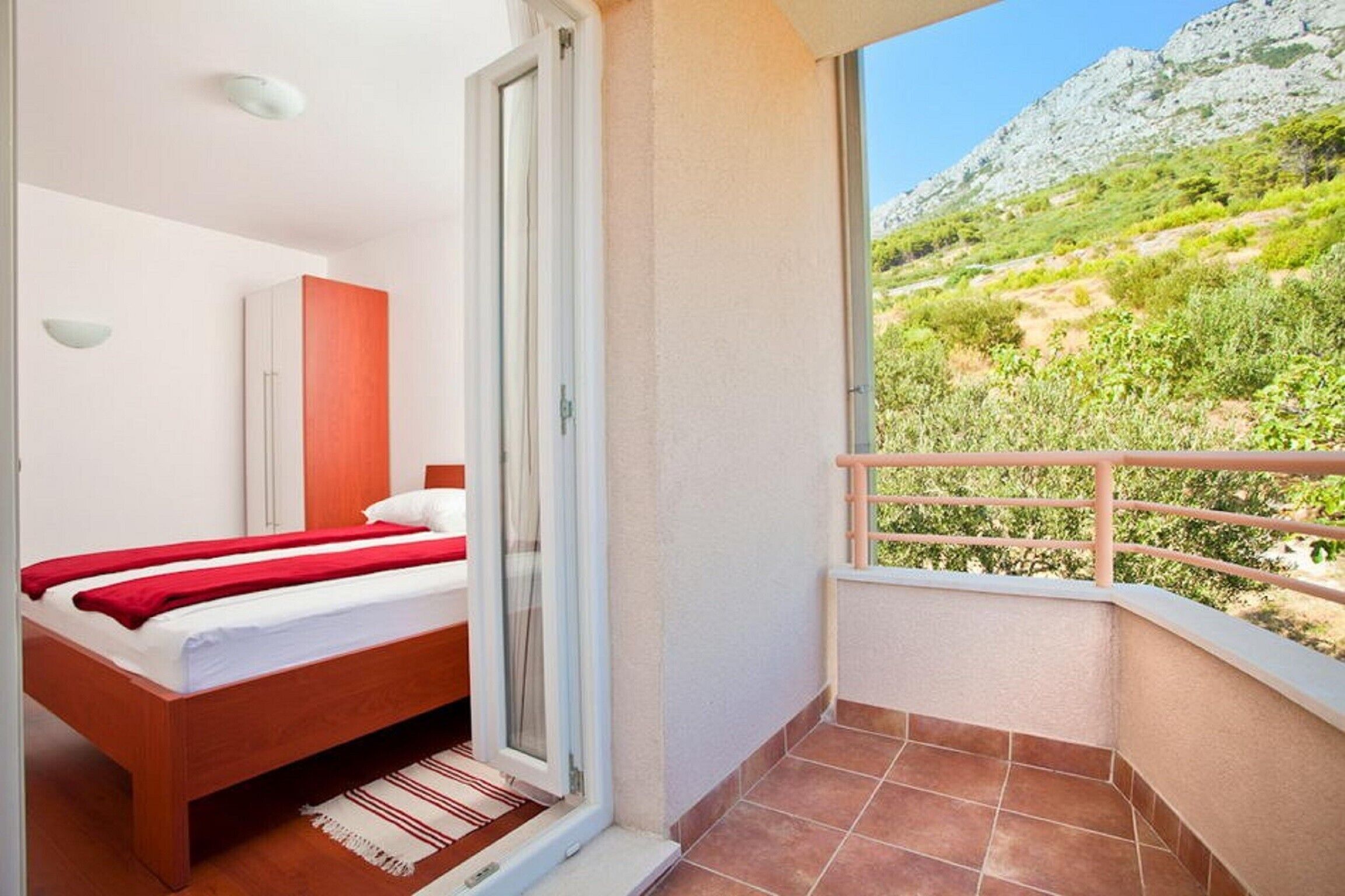 A bedroom with a bed, a wardrobe, and a sliding glass door leading to a balcony with a view of a mountainous landscape. - Apartments Relax Brela - Two Bedroom Apartment (Brela)