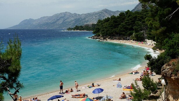 A beach with clear turquoise waters, people sunbathing, and a mountainous backdrop. - Apartments Relax Brela - Two Bedroom Apartment (Brela)