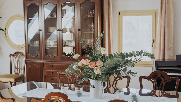 A dining room with a wooden cabinet, a table with chairs, and a vase with flowers. - Enchanted Misty Valley Cottage Apartments - Standard One Bedroom Apartment (Sentjost nad Horjulom)