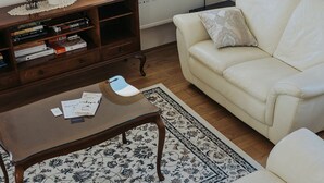 A living room with a white sofa, a wooden coffee table, a patterned rug, and a bookshelf with books and decorative items. - Enchanted Misty Valley Cottage Apartments - Standard One Bedroom Apartment (Sentjost nad Horjulom)