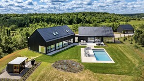 A modern house with a large glass facade, a swimming pool, and a well-maintained lawn.