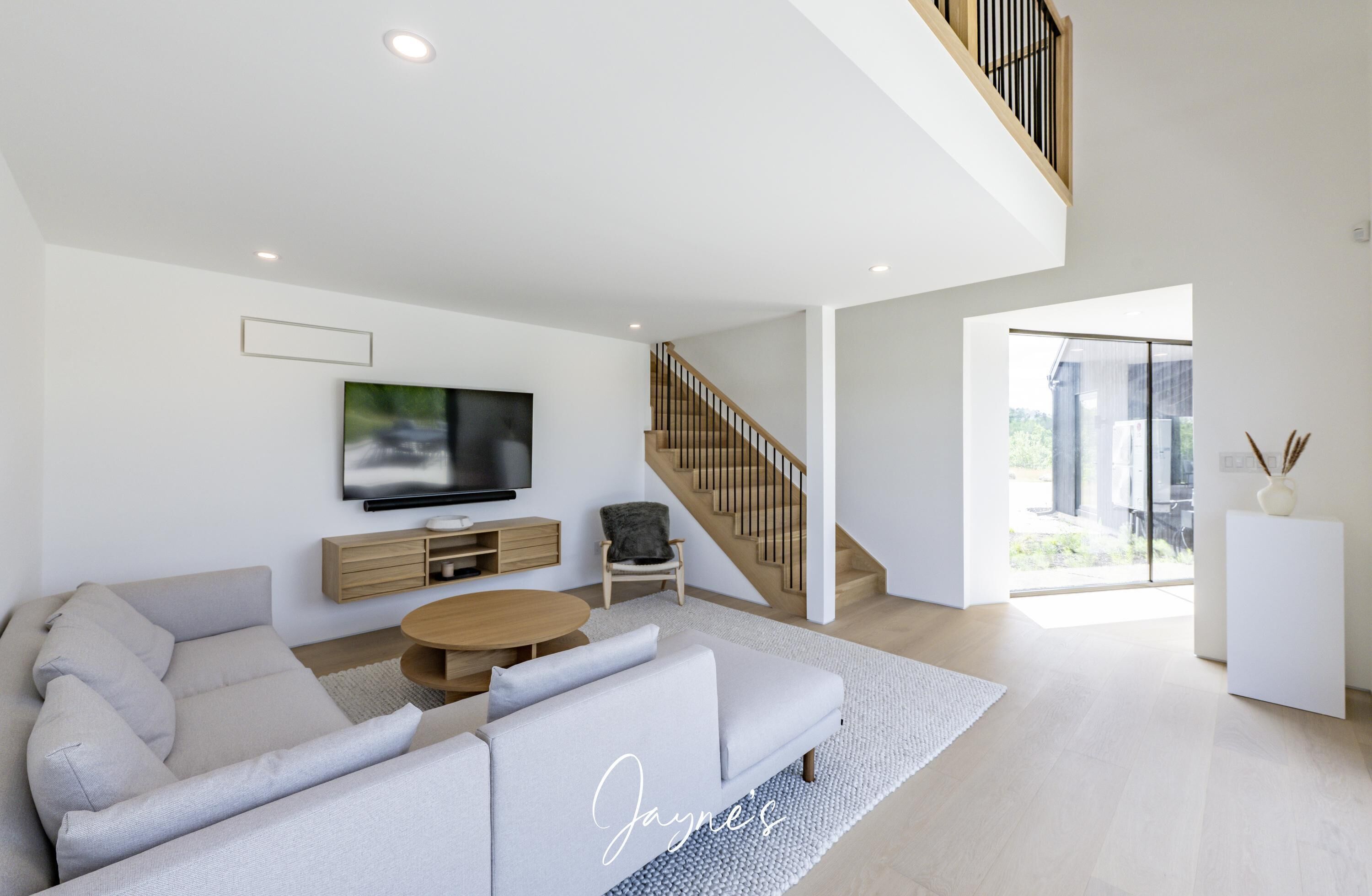A modern living room with a sofa, coffee table, TV, and a staircase leading to an upper level.