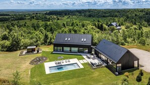 A modern house with a large glass facade, a swimming pool, and a well-maintained lawn.