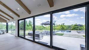 A spacious interior with large sliding glass doors leading to an outdoor patio area with a pool and lounge furniture.