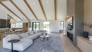 Una sala de estar moderna con un sofá seccional grande, un comedor con muebles de madera y una cocina al fondo.