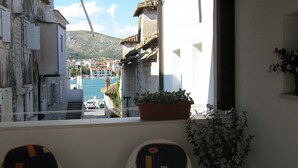A balcony with a table and chairs, overlooking a harbor with buildings and a hill in the background. - Klaudija’s Charming Apartments & Rooms - Room 4 (Trogir)