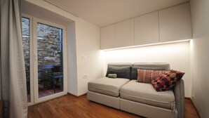 A compact living space with a sofa, a small table, and a sliding glass door leading to an outdoor area.
