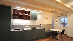 Una cocina moderna con encimera de granito, armarios verde oscuro y una mesa de comedor blanca con sillas negras.