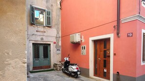 Una calle estrecha con una moto estacionada frente a un edificio de fachada roja y puerta verde.