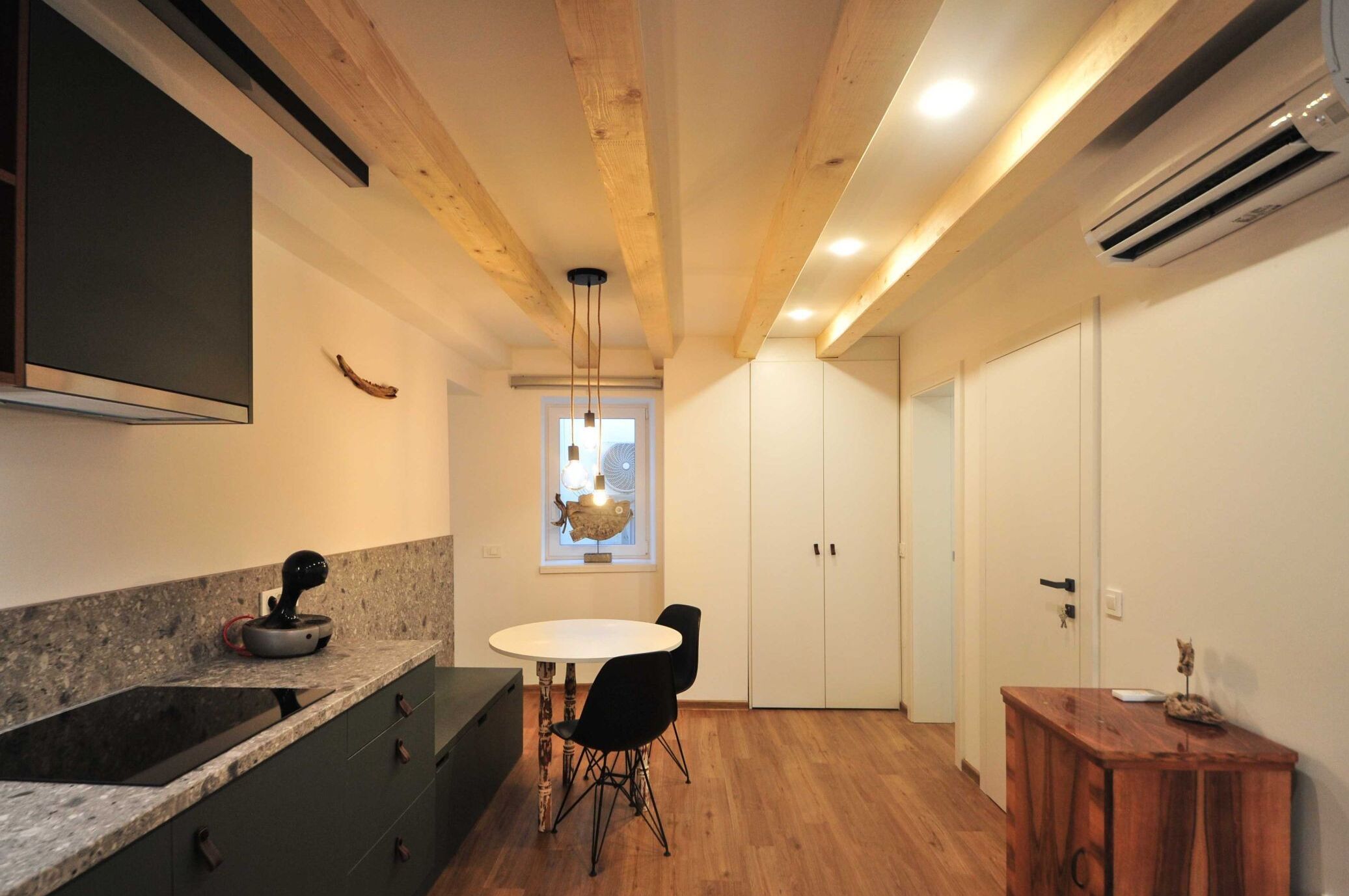Una cucina moderna con un piano di lavoro in granito, un tavolo da pranzo con sedie, travi in legno al soffitto e un condizionatore d'aria.