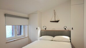 Un dormitorio con cama, ventana, luz empotrada y una pequeña vela decorativa.