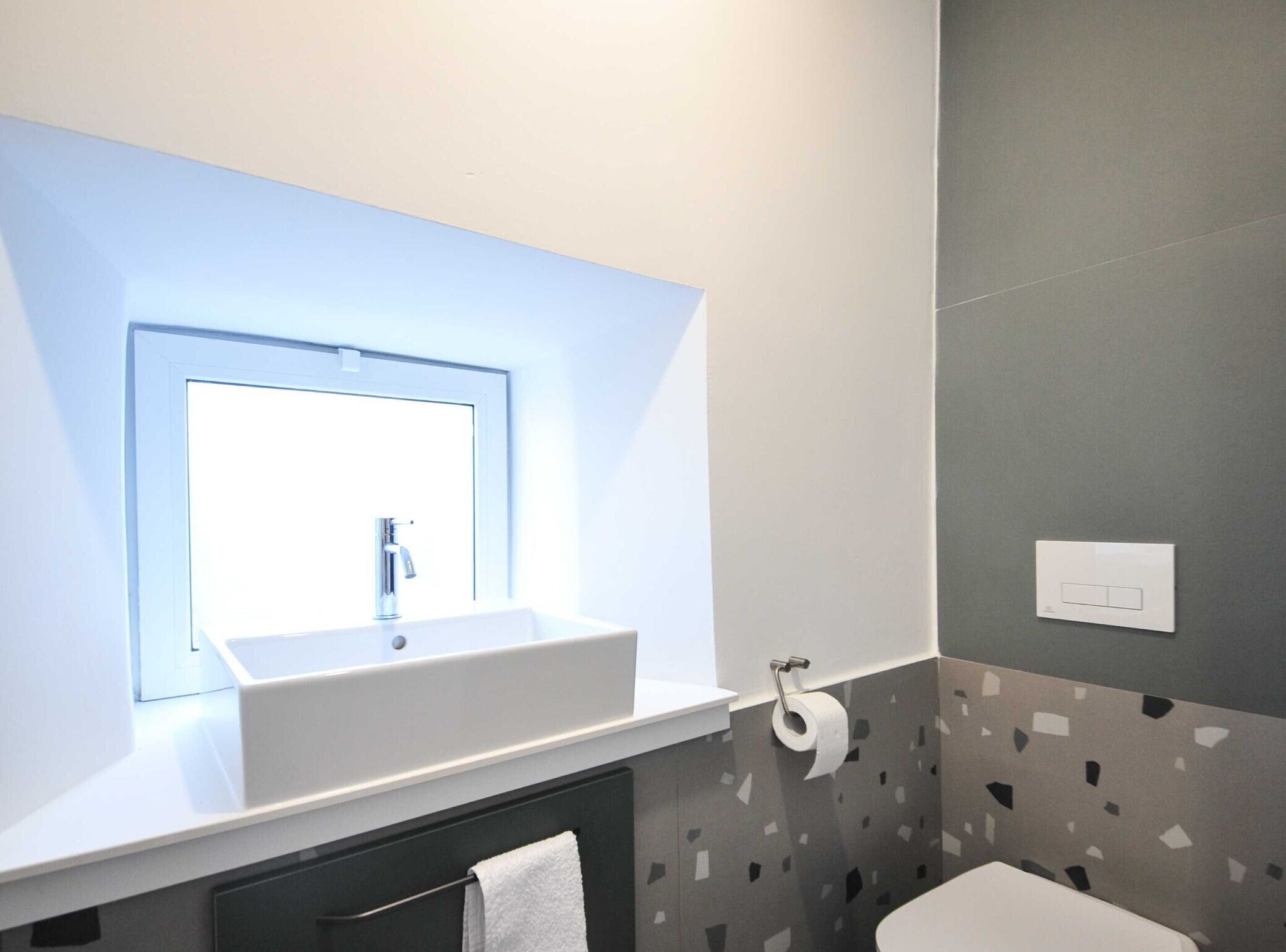 A modern bathroom with a white sink, a mirror, a toilet, and a towel rack.