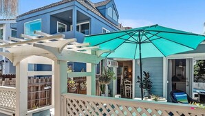 A blue house with a covered patio area, a white pergola, and a turquoise umbrella.