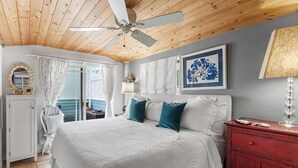 A bedroom with a wooden ceiling, a bed with white and teal bedding, a red dresser, a white cabinet, and a framed artwork on the wall.