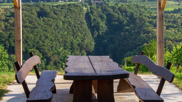 A wooden pergola with a picnic table and benches overlooking a lush valley.