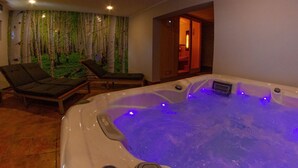 A spa area with a hot tub, two lounge chairs, and a wall with a forest mural.