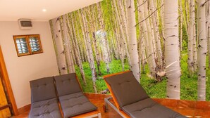 A room with two wooden-framed lounge chairs with grey cushions, a large window, and a wall mural of birch trees.