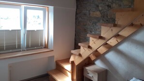 Un escalier en bois, un mur en pierre et une fenêtre avec des stores.