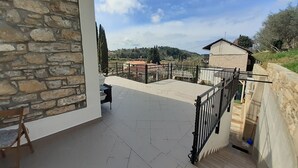 Un balcon aux murs en pierre, doté d’un sol carrelé et offrant une vue sur un paysage rural avec des maisons et des arbres.