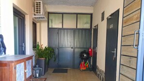 A narrow hallway with a tiled floor, a wooden bench, a potted plant, a grill, and a door with a sign.