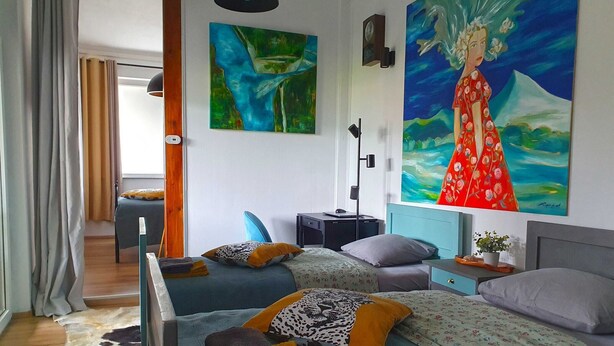 A modern hotel room with two beds, a desk, a chair, and artwork on the walls.
