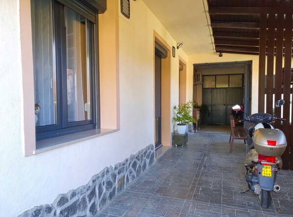 A narrow paved corridor with a scooter parked on the right, a potted plant, and a wooden bench.