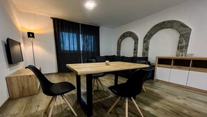 Ett modernt vardagsrum med ett matbord i trä, svarta stolar, en svart soffa, en valvformad öppning i sten och en tv som är monterad på väggen.