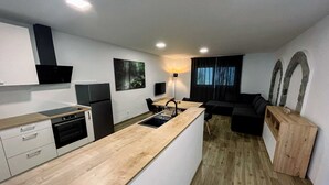 Ett modernt kök med en bänkskiva i trä, inbyggda vitvaror och en matplats med en svart soffa och en träskommod.