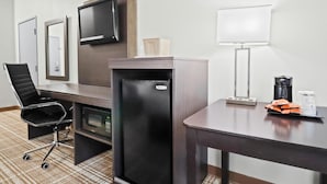 A hotel room with a desk, a black office chair, a minibar, a television mounted on the wall, a lamp, and a coffee maker. - GrandStay Hotel & Suites  (Minocqua)