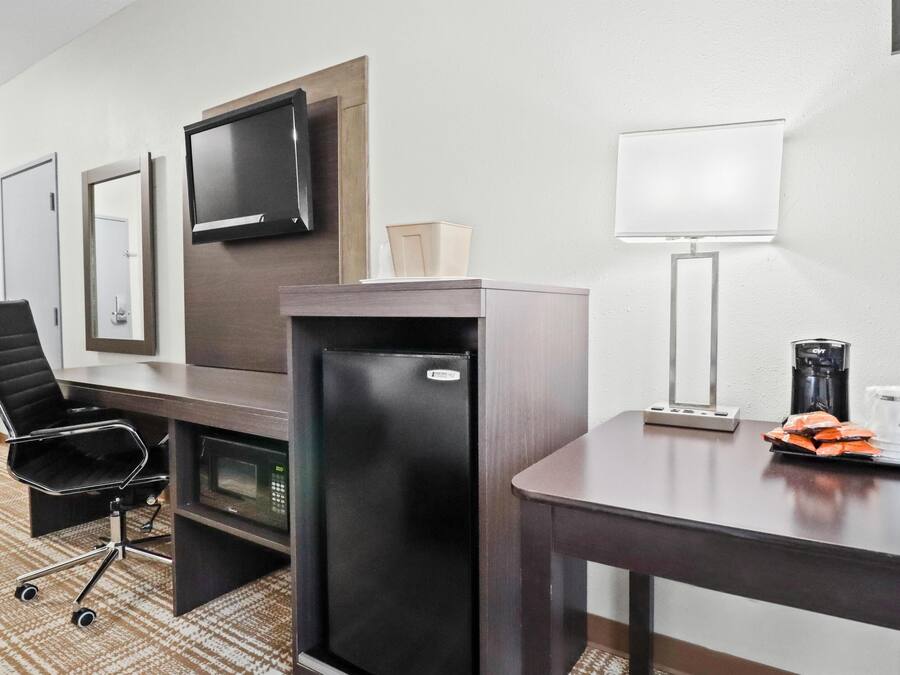 Une chambre d’hôtel équipée d’un bureau, d’un fauteuil de bureau noir, d’un mini-bar, d’un téléviseur fixé au mur, d’une lampe et d’une machine à café.