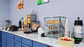 A breakfast bar with waffle makers, a coffee machine, and a glass display case with pastries. - GrandStay Hotel & Suites  (Minocqua)