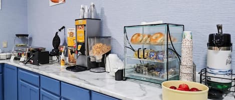 Eine Frühstückstheke mit Waffeleisen, einer Kaffeemaschine und einer Glaskuppel mit Gebäck.