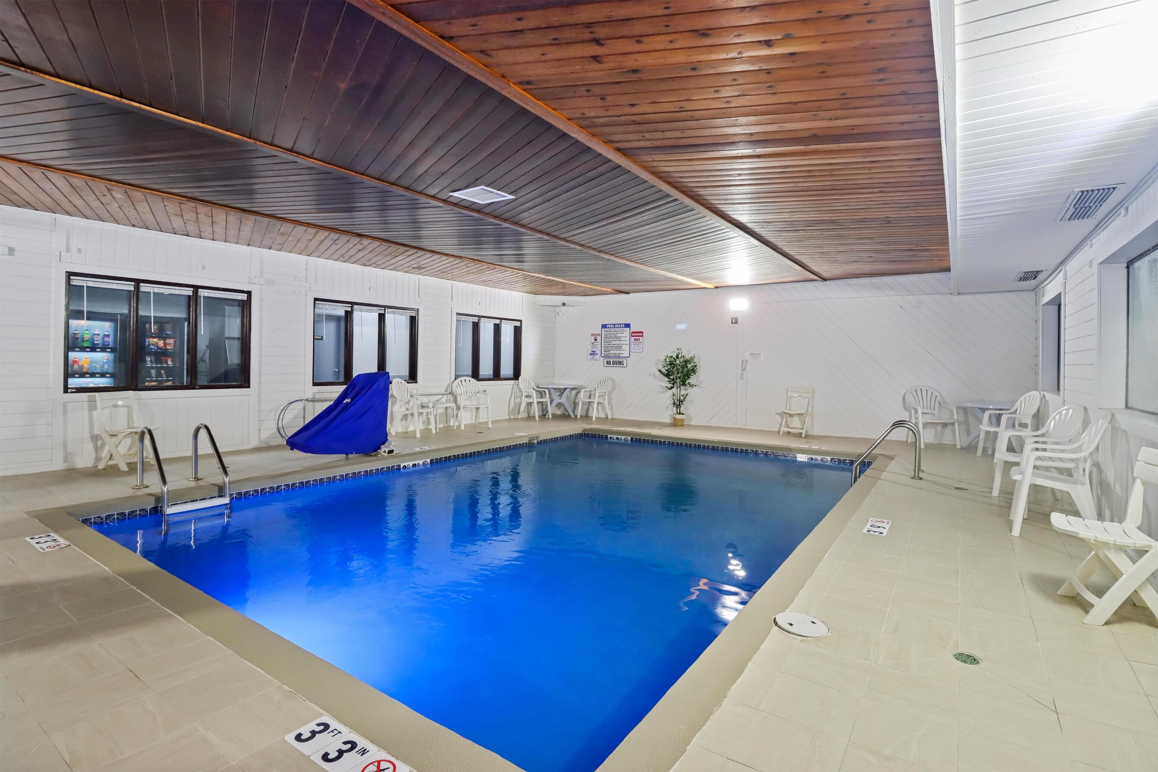 An indoor swimming pool with a wooden ceiling, white walls, and a blue pool.
