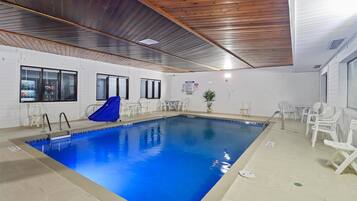 Una piscina interior con techo de madera, paredes blancas y agua azul.