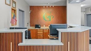 A reception area with a wooden panel wall, a large G logo, and a flag. - GrandStay Hotel & Suites  (Minocqua)