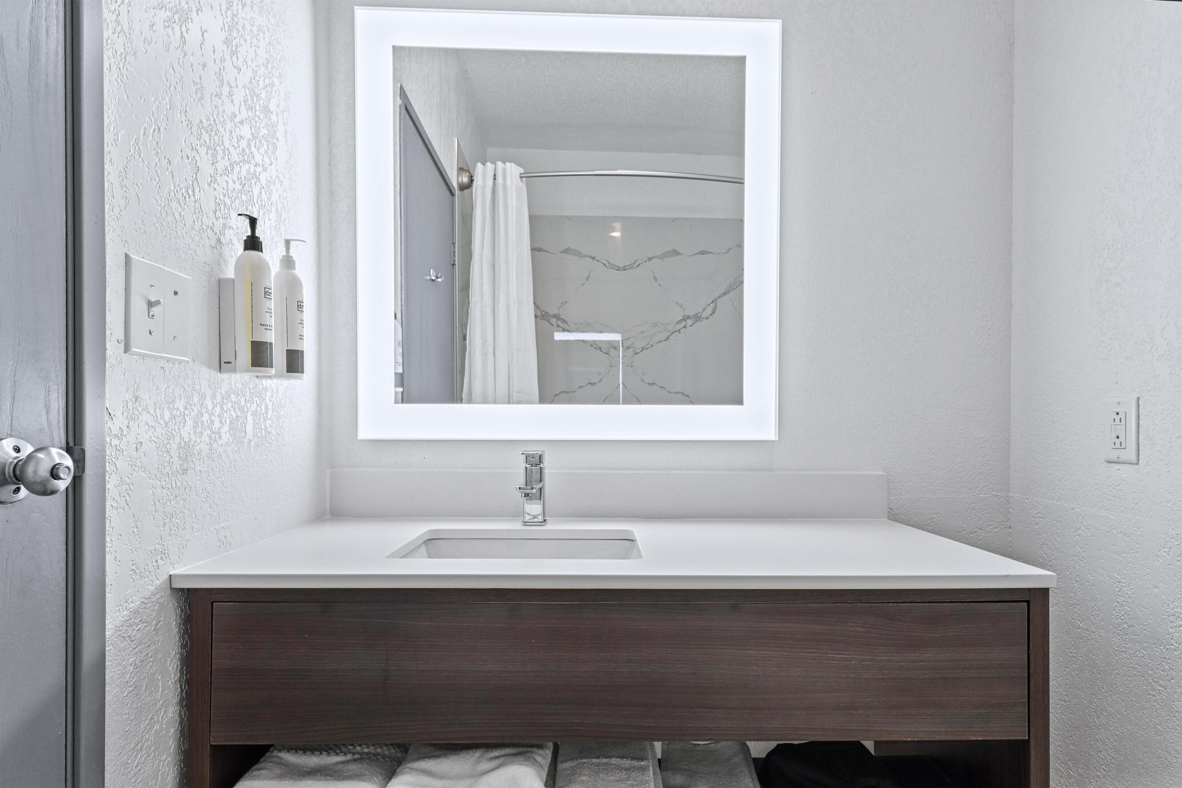 Un baño moderno con un lavamanos blanco, tocador de madera oscura y un espejo grande.