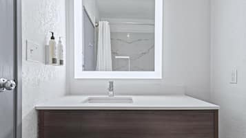 Un baño moderno con un lavamanos blanco, tocador de madera oscura y un espejo grande.