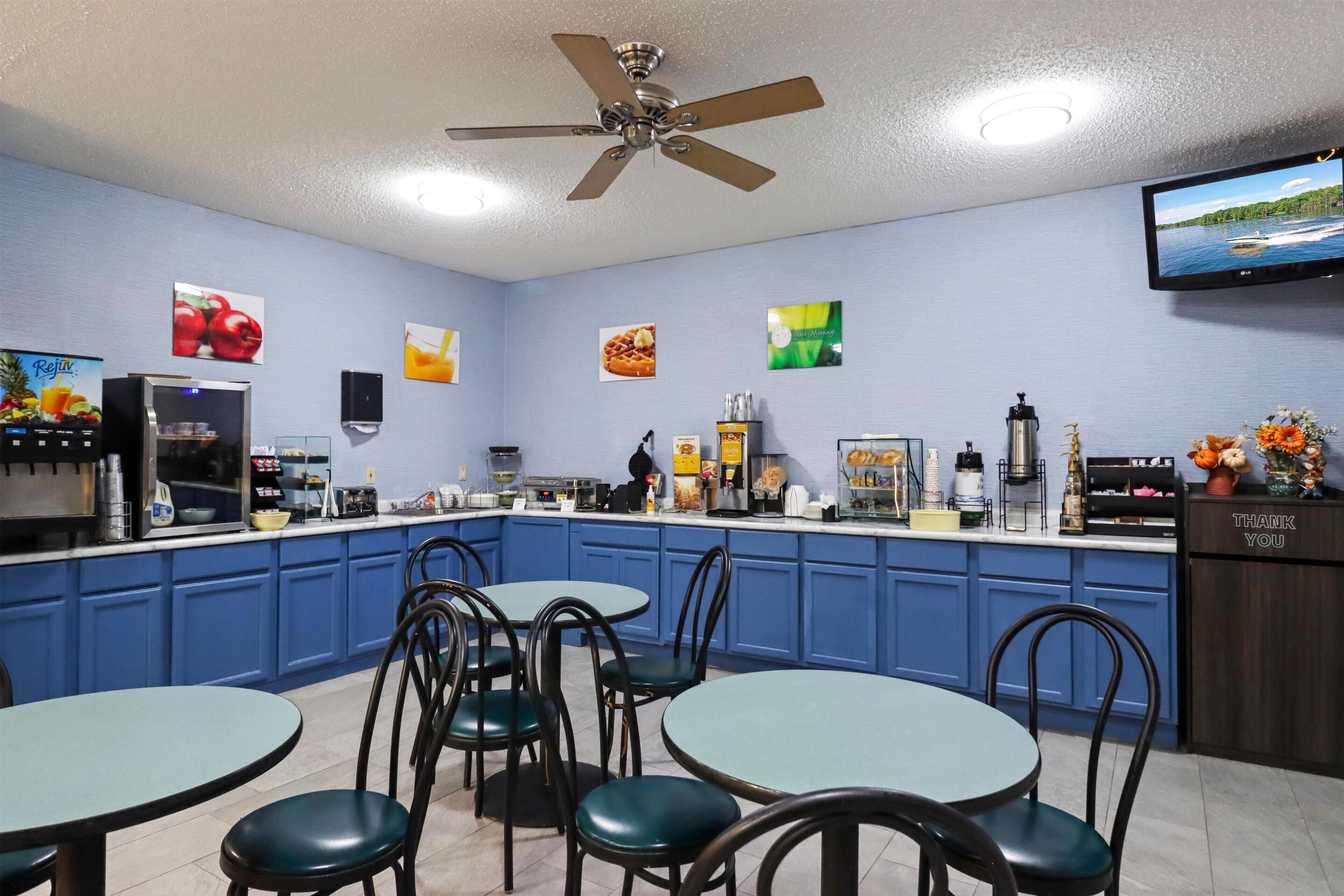 A restaurant with blue cabinets, a counter with various food items, and a television mounted on the wall.