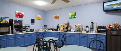 A restaurant with blue cabinets, a counter with various food items, and a television mounted on the wall.