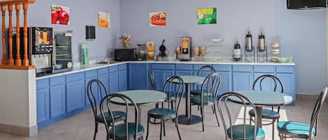 A modern kitchen with blue cabinets, a central island with a coffee machine, and a seating area with metal chairs and tables.